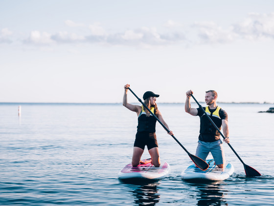 Man and woman wearing life jackets while paddleboarding on lake.