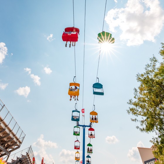 Several people seated on Sky Glider ride above the ground at state fair with sun and blue skies in background 