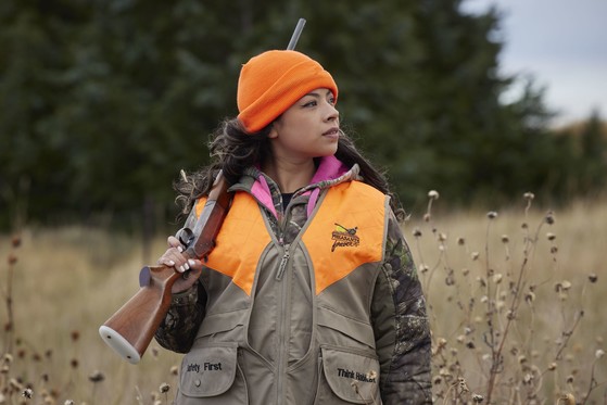 female hunter wearing blaze orange carrying rifle through field