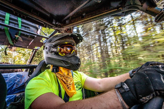 Man wearing helmet, safety glasses and gloves driving UTV through forest