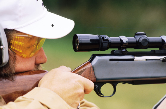 A hunter looks through their scope while wearing eye and ear protection