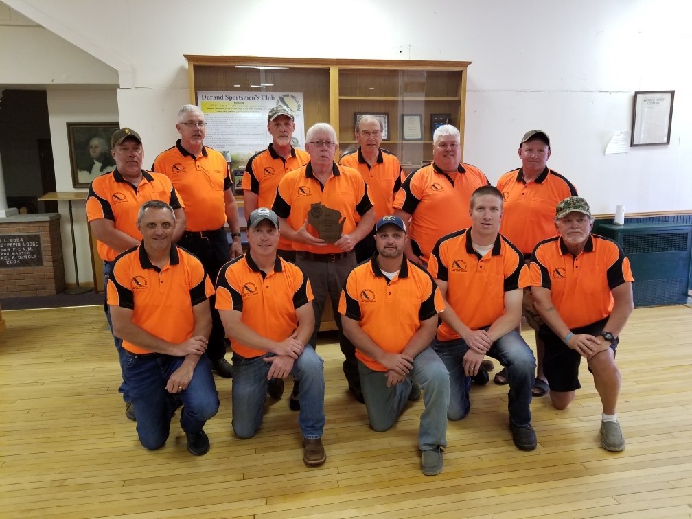 Male hunter education instructors wearing orange and black shirts pose in three rows for group picture after winning award.