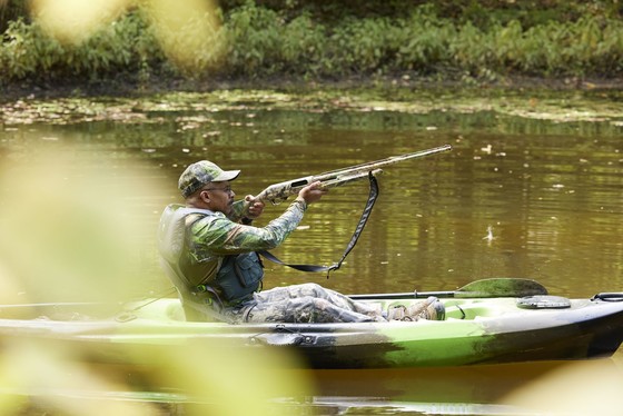 A man in a kayak wearing hunting gear.