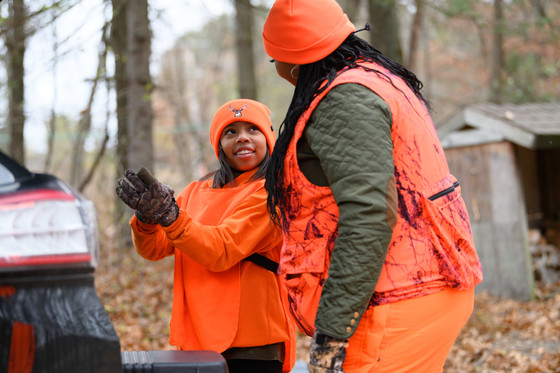 a young woman wearing blaze orange chatting with a mentor wearing blaze orange preparing to hunt