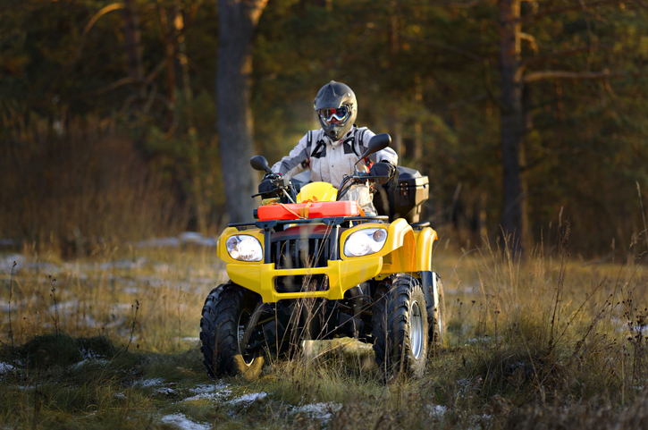 man in helmet and safety goggles looking into the camera while sitting on ATV against snowy late autumn landscape.