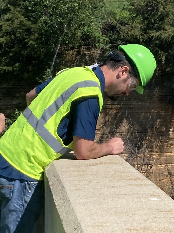 A dam engineer looking down over a concrete barrier and inspecting a dam.