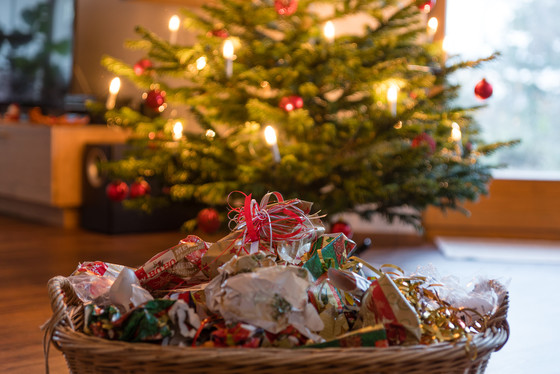 Balls of torn-up wrapping paper in a basket in front of a decorated Christmas tree.