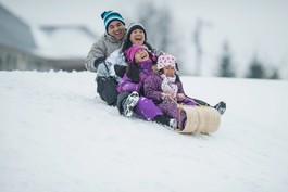 A family smiling while sledding down hill