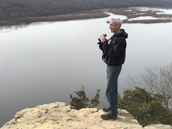 Thomas Meyer standing on a rock overlook, holding binoculars and looking into the distance.