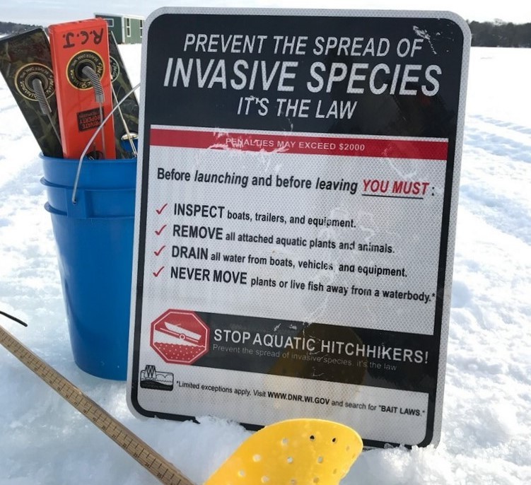 A photo of a sign on a frozen, snow-covered that says, "Prevent the spread of invasive species - it's the law."