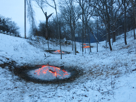 Image of brush piles reduced to red hot coals covered with gray ash. The four scattered burn piles are surrounded by snow and scattered trees released by the brush removal efforts.