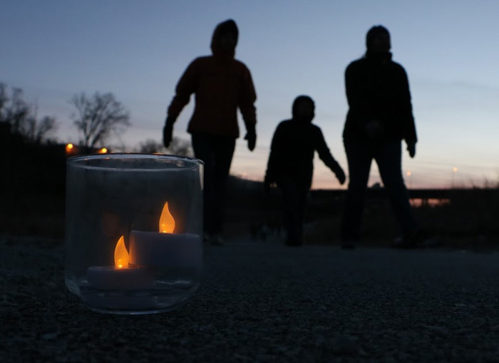 The silhouette of a family walking at dusk on a candlelit trail.