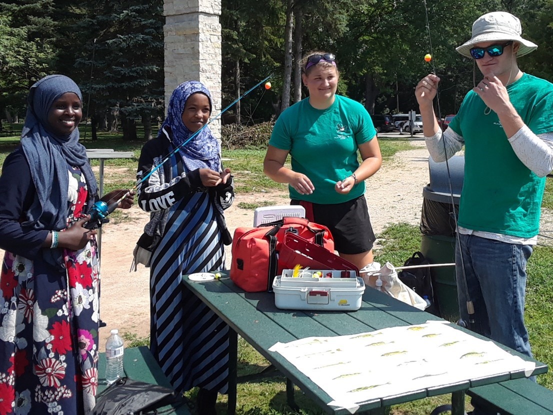 two women wearing hijabs stand across from 2 DNR staff as they learn how to fish