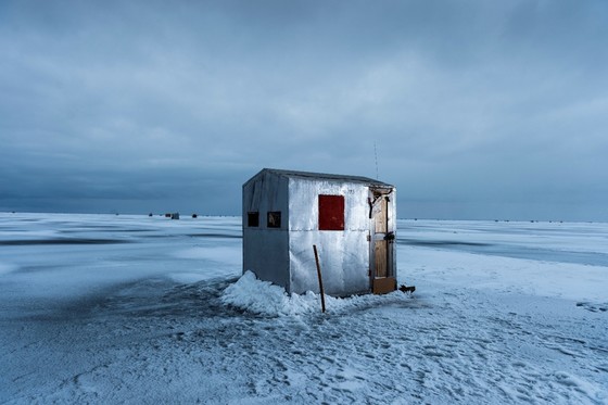 A silver ice shanty is the focal point on a snow and ice-covered lake.