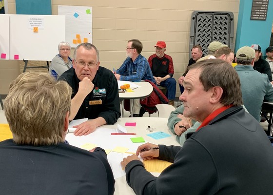 John pohlman seated at a table talking with two other people