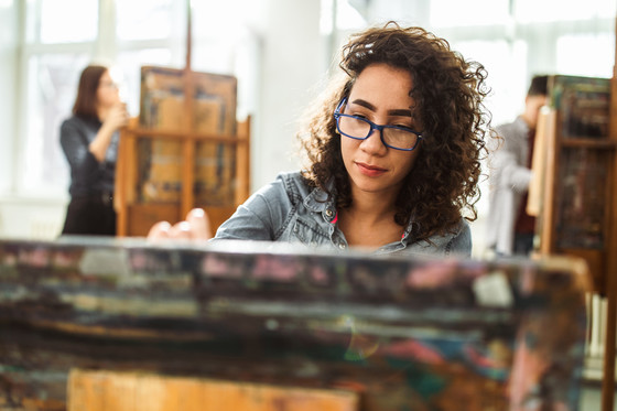 African American female student with blue glasses drawing on a canvas during a class at school