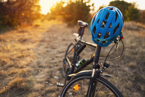 A closeup of a black bike with a blue helmet hanging on the handle bar in a nature area in early spring.