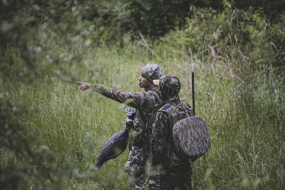 two men in camo walking in the woods