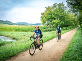 Bike riders on a gravel trail pass through farm fields