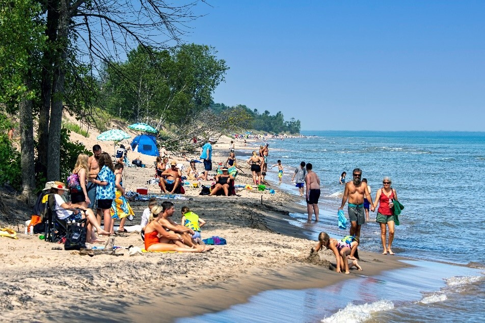 A crowd of people enjoy a sunny summer day at the beach of Kohler Andrea State Park.