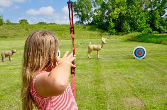 Girl shooting a bow and arrow towards a target