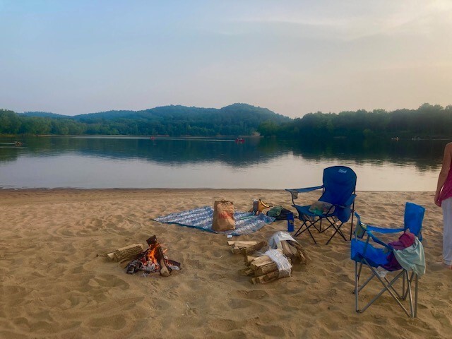 Campfire and camp chairs on sandy beach in front of river