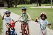 Three kids on bicycles wearing bike helmets and smiling
