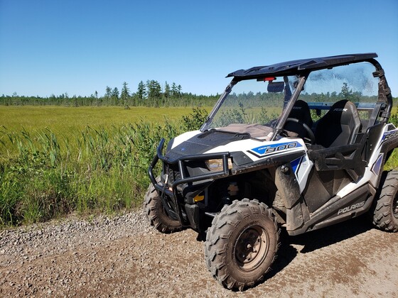 A UTV parked on a gravel trail next to a green field.