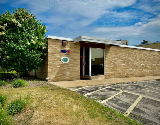 a light brown brick building with a blue sky and a green tree on the left