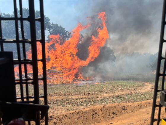 Flames take over brush and the leaves of trees as seen from heavy equipment building a fire break.