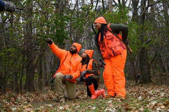 dad wearing hunting gear pointing to sky with mother and daughter looking on