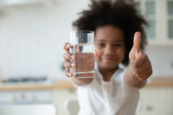 Focus on happy small african american girls hands holding glass with fresh pure water and showing thumbs up gesture.