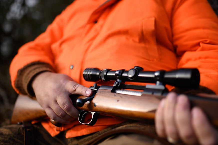 A hunter wearing a blaze orange vest waits in a camouflaged blind. 