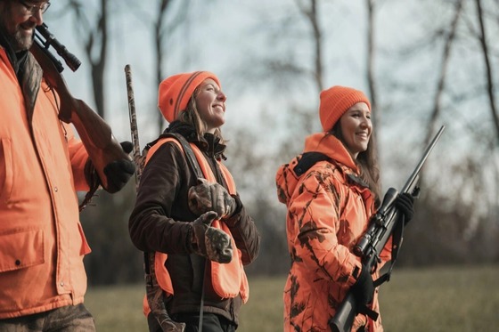 Three hunters, all in blaze orange, smiling as they walk through a field. 