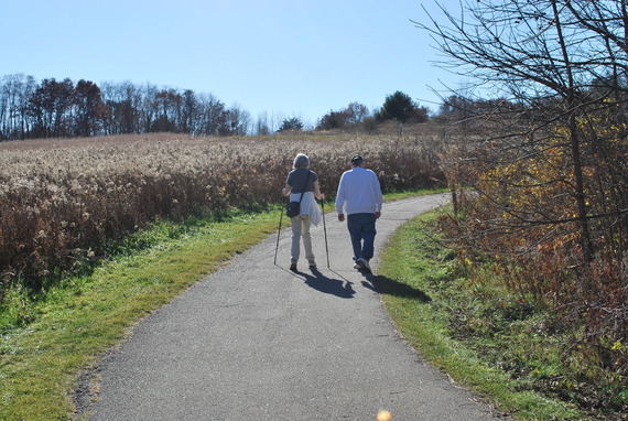 Two people, one with mobility assistance, walking on a gravel trail outside