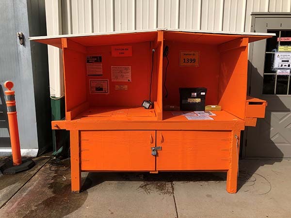 An orange kiosk sits on concrete outside a metal building.