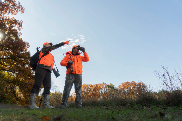 man and woman wearing blaze orange hunting at edge of a field