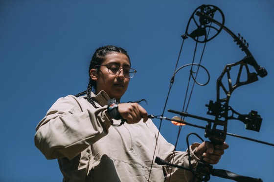 A young adult knocks an arrow onto their bow at a shooting range.