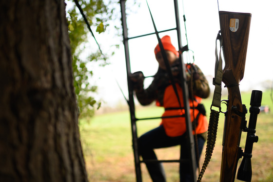 gun in a sling being carried up a deer stand