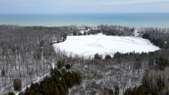 A drone view of Harrington Beach State Park in the winter with snow, blue water and trees