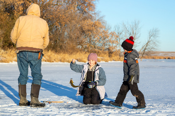 A young girl holds up a perch she caught ice fishing with her family. 