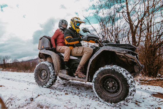 Two ATV riders wearing helmets navigate a snow-covered trail. 