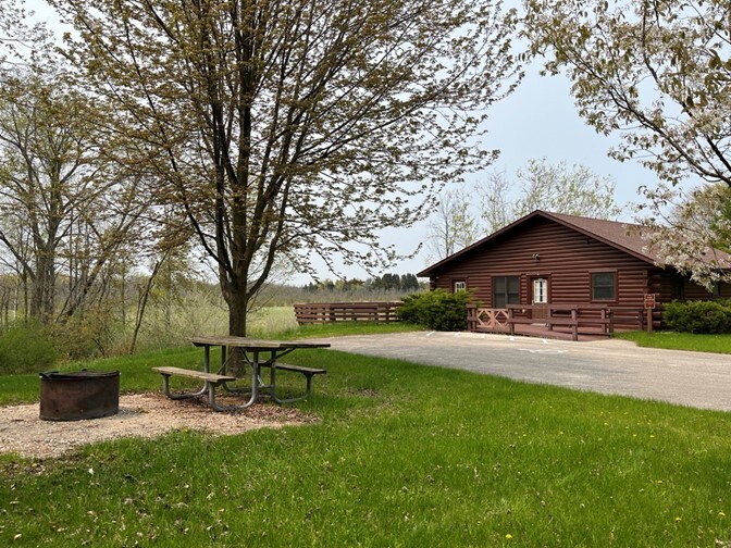 A brown cabin with a wheelchair ramp leading to its front door sits next to a prairie at Kohler-Andrae State Park. 