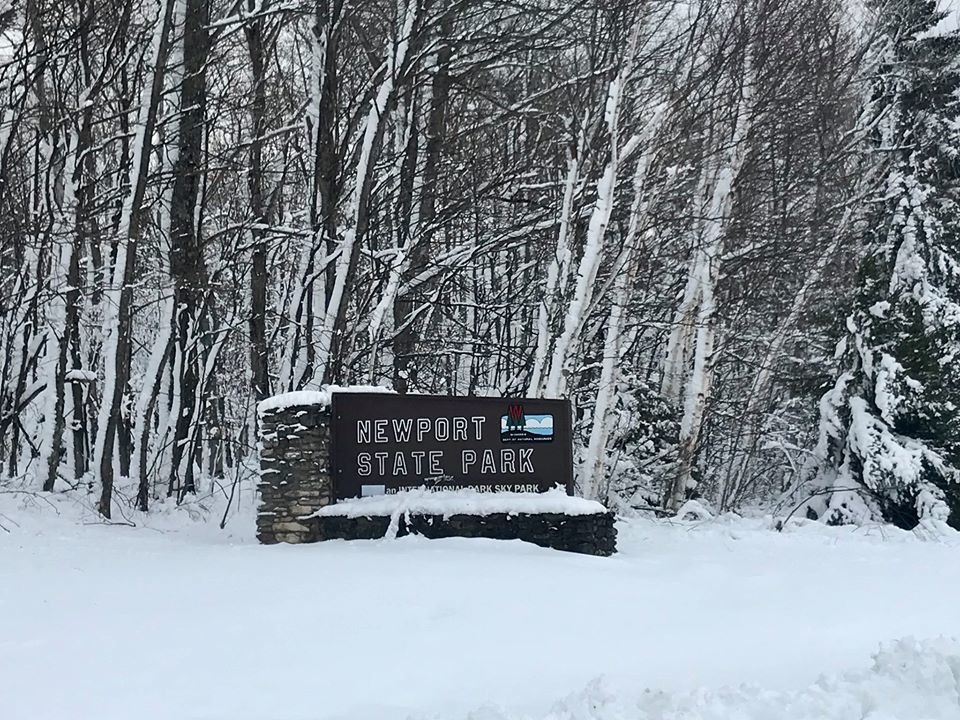 The entrance sign for Newport State Park with a snowy wooded area behind it. Snow covers the ground. 