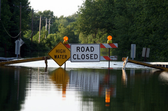 Signs reading "high water" and "road closed" block a flooded road from traffic. 