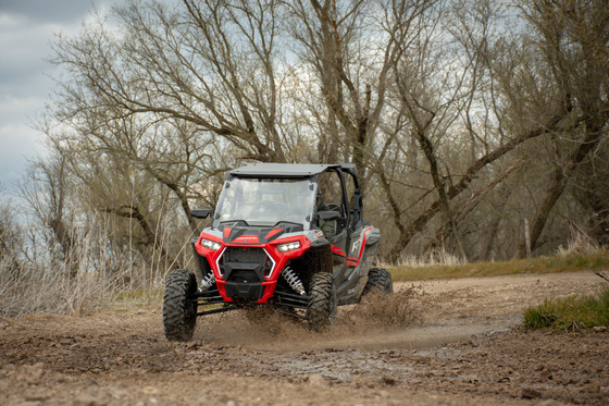 A UTV rides through a puddle on a muddy trail. 