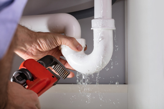 A hand holding a pipe wrench fixes a leaky PVC pipe. 