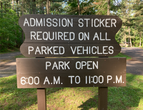 wooden sign that says "admission sticker required on all parked vehicles, park open 6 a.m. - 11 p.m.