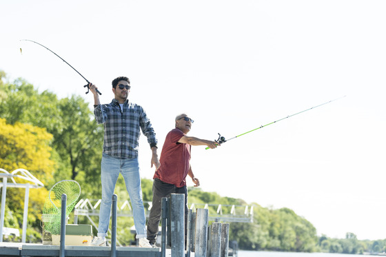 Two men stand on a dock and cast fishing rods into the water. 