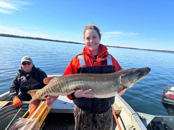 a woman holding a musky with a man on a boat